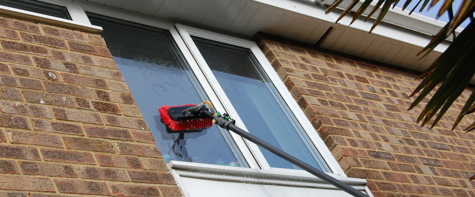 Picture of an operative cleaning windows with a brush, feed with pure water - the method we use at Masterclean2